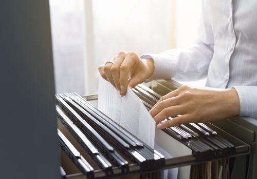 Professional female office clerk searching files and paperwork in the filing cabinet